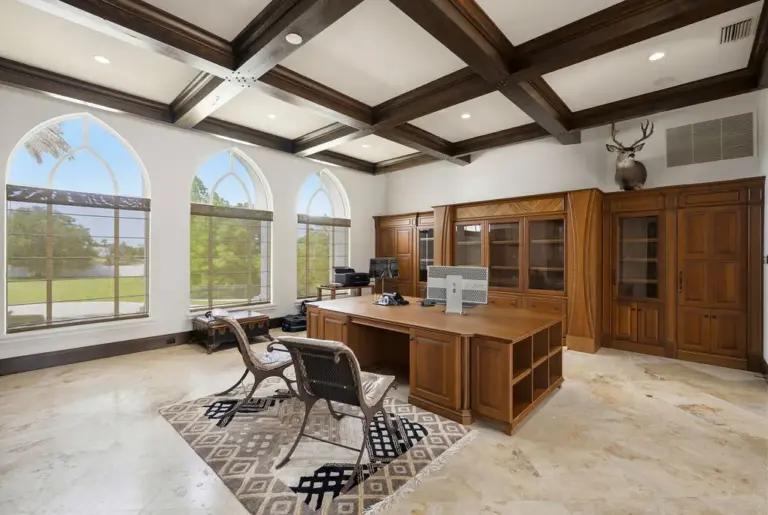 A spacious home office features custom cabinetry and wood coffered...