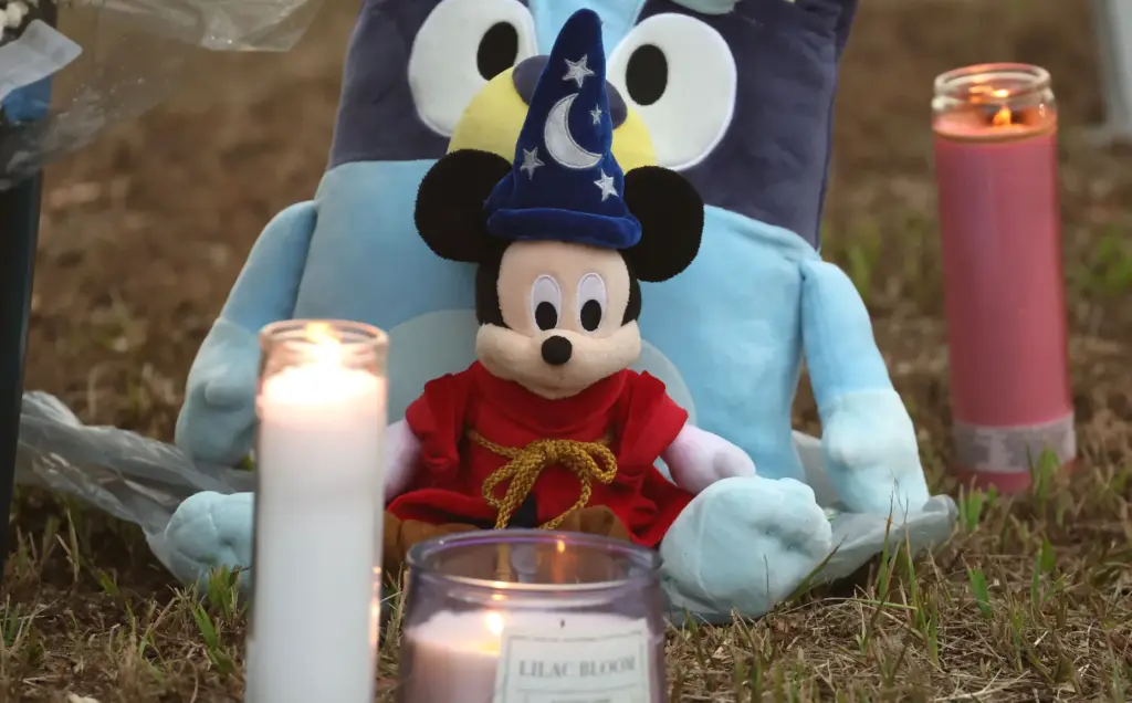 Stuffed animals and lighted candles rest in the lawn during...