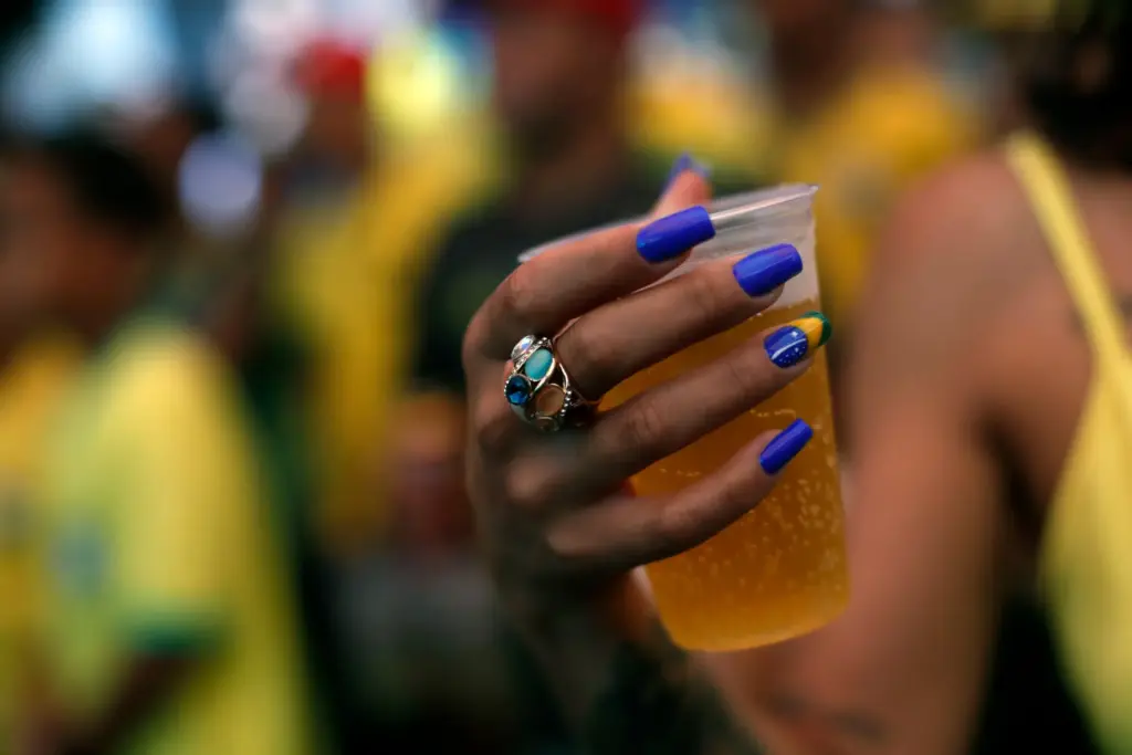 A soccer fan, with nails painted with a Brazil flag, holds a beer.