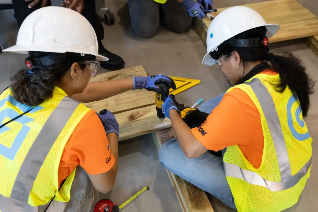 Campers work together to drill in screws to build a...