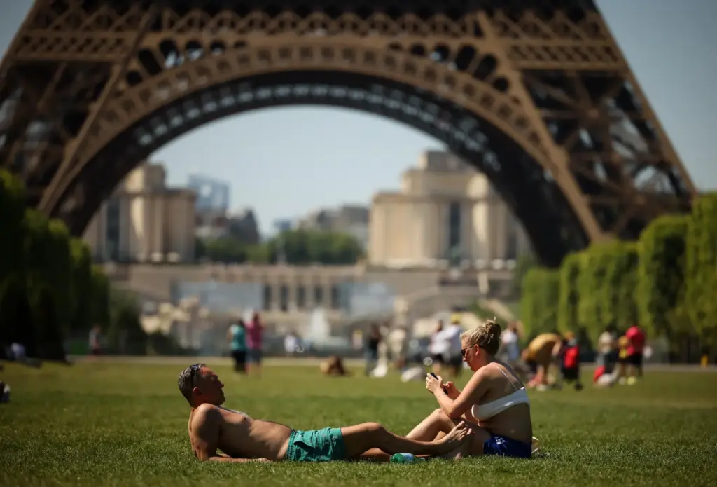 People enjoy the sun next to the Eiffel Tower.