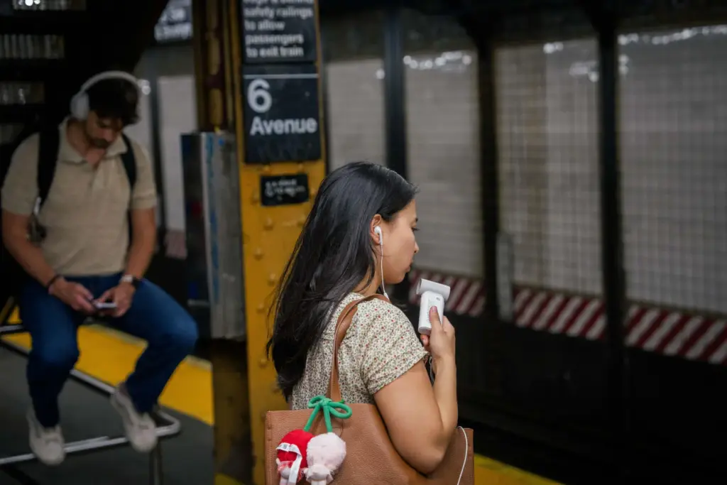 A person uses a mini electric fan as they wait on a New York subway platform.
