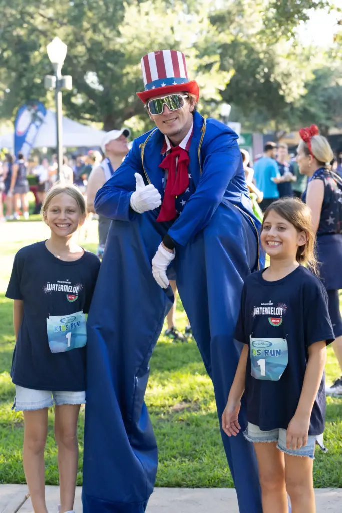 Runners take a photo with Uncle Sam on stilts during...