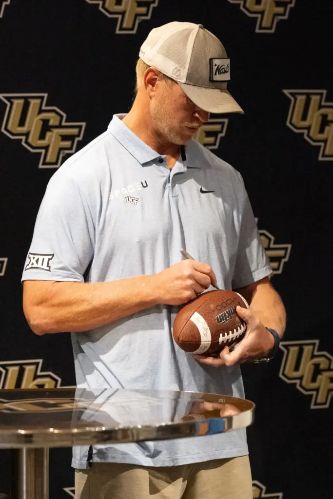 Knightâs Football Coach Scott Frost signs a fanâs football during...