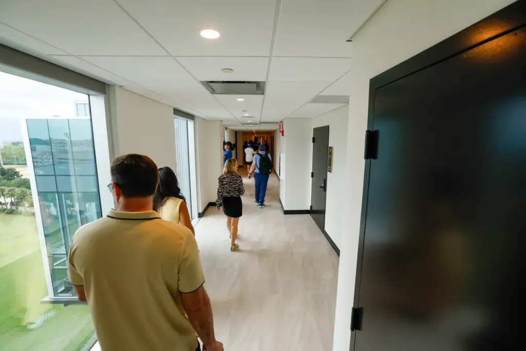 A hallway lined with floor-to-ceiling windows leads to the various...