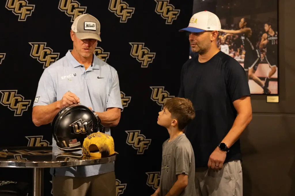 Knightâs Football Coach Scott Frost signs a fanâs helmet during...