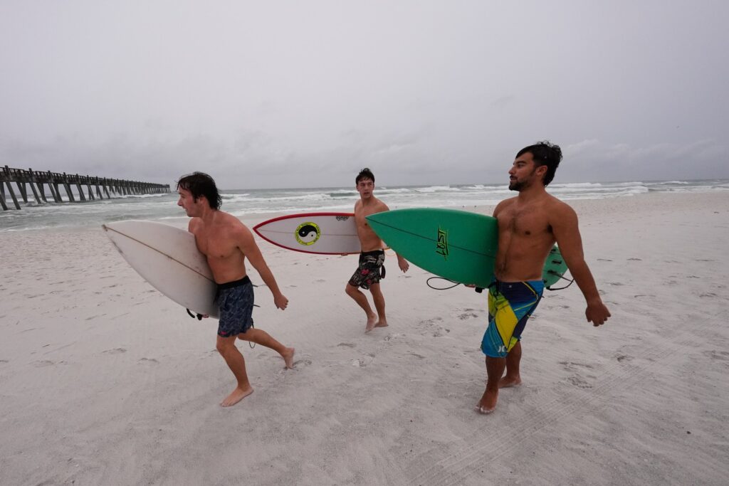 Surfers walk along the beach as Hurricane Isaias approaches Pensacola...