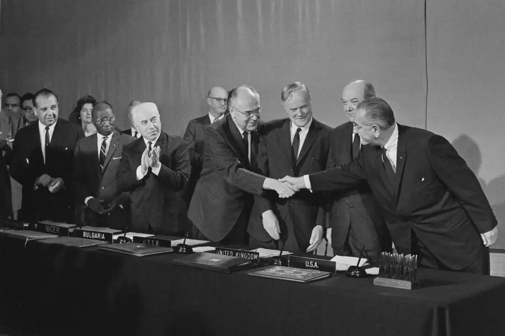 FILE – U.S. President Lyndon Johnson, right, reaches over to...